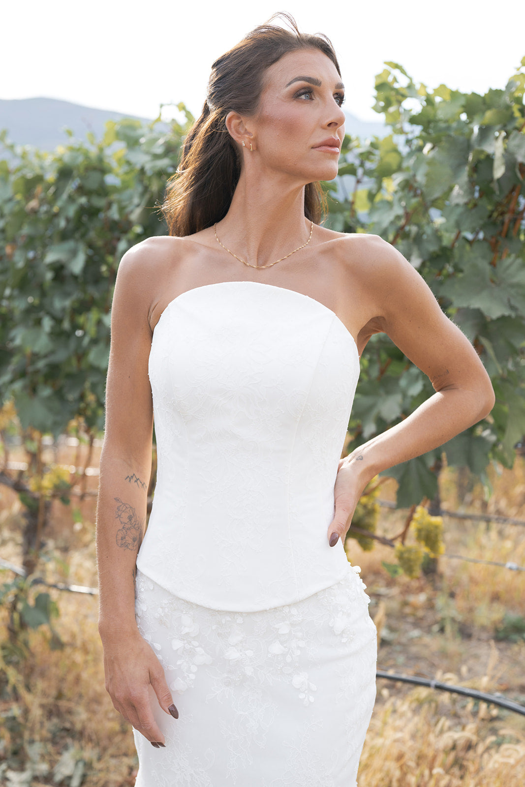 Woman in a white strapless dress with Round neckline and structured fit standing in a vineyard.  Amanti by Le Reve Boutique. St. Alberta, Alberta