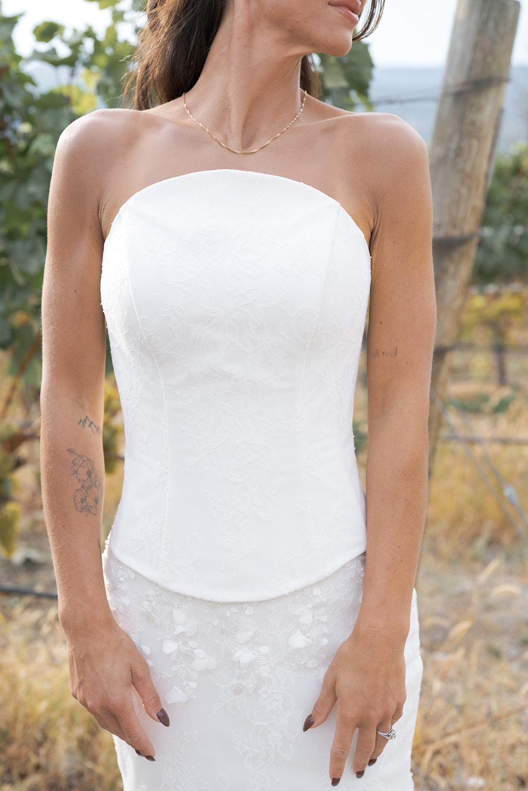 Woman wearing a strapless white Satin corset dress with exposed boning with a blurred natural background. Amanti by Le Reve Boutique.  St. Albert, Alberta