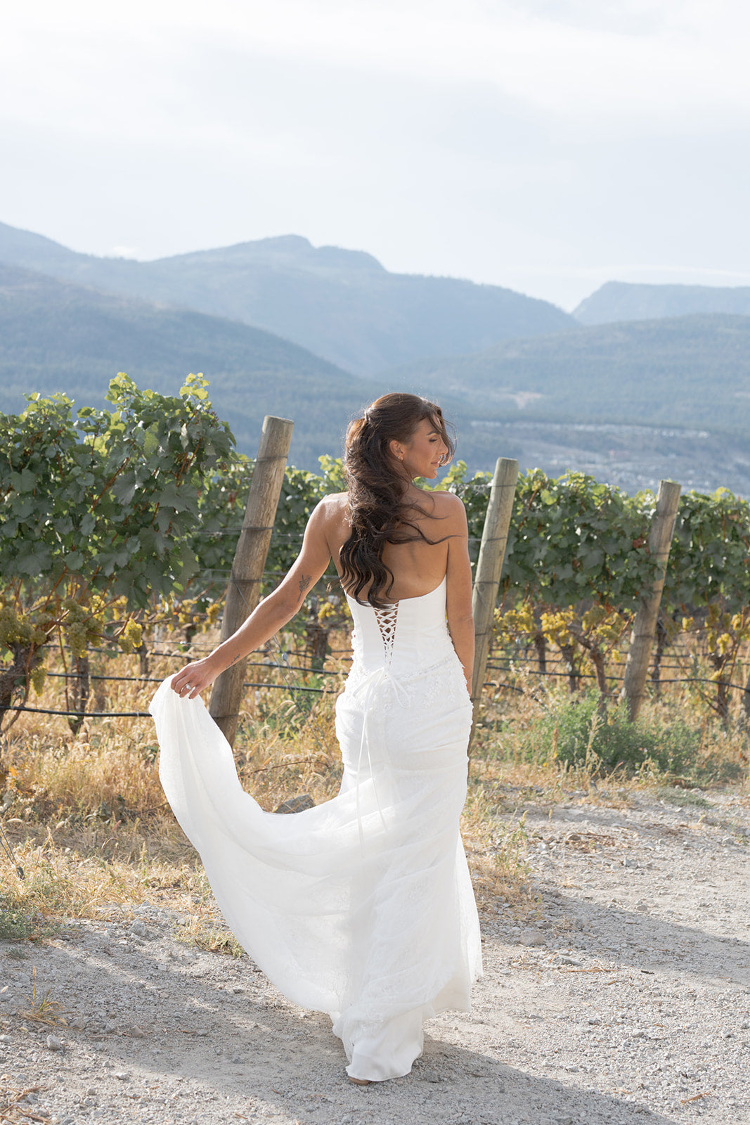 Woman in an Amanti Fiorina Set Two-piece bridal set: satin bodice + Chantilly lace skirt white wedding dress standing in a vineyard with mountains in the background.  Le Reve Boutique