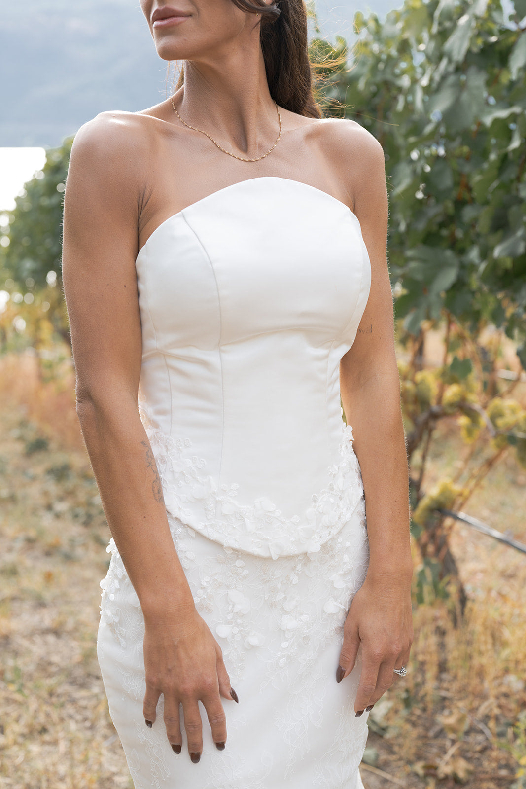 Woman wearing an Amanti Fiorina Set strapless white Soft floral Chantilly lace skirt with romantic texture wedding dress in an outdoor setting with greenery.  Le Reve Boutique Edmonton, Alberta