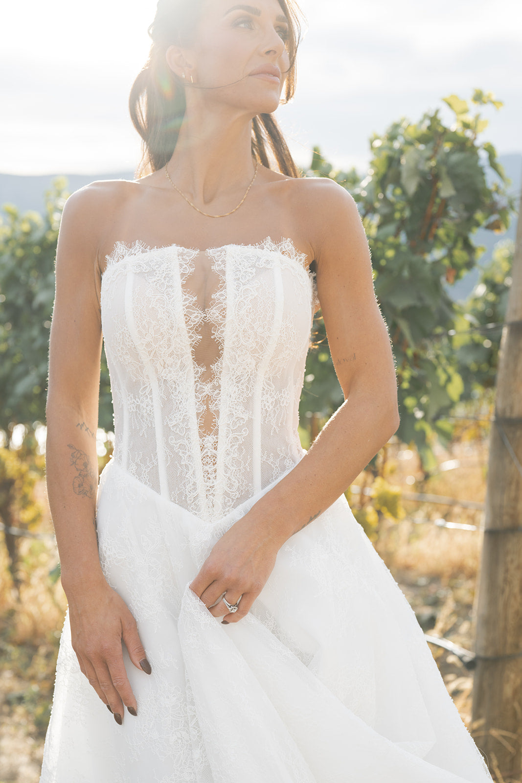 Woman in Amanti Fortuna white wedding dress with Straight across neckline with keyhole detail, Basque waistline for a flattering, elongated shape, A-line silhouette in Chantilly French lace wedding dress standing in a outdoor setting. Le Reve Boutique St. Albert, Alberta