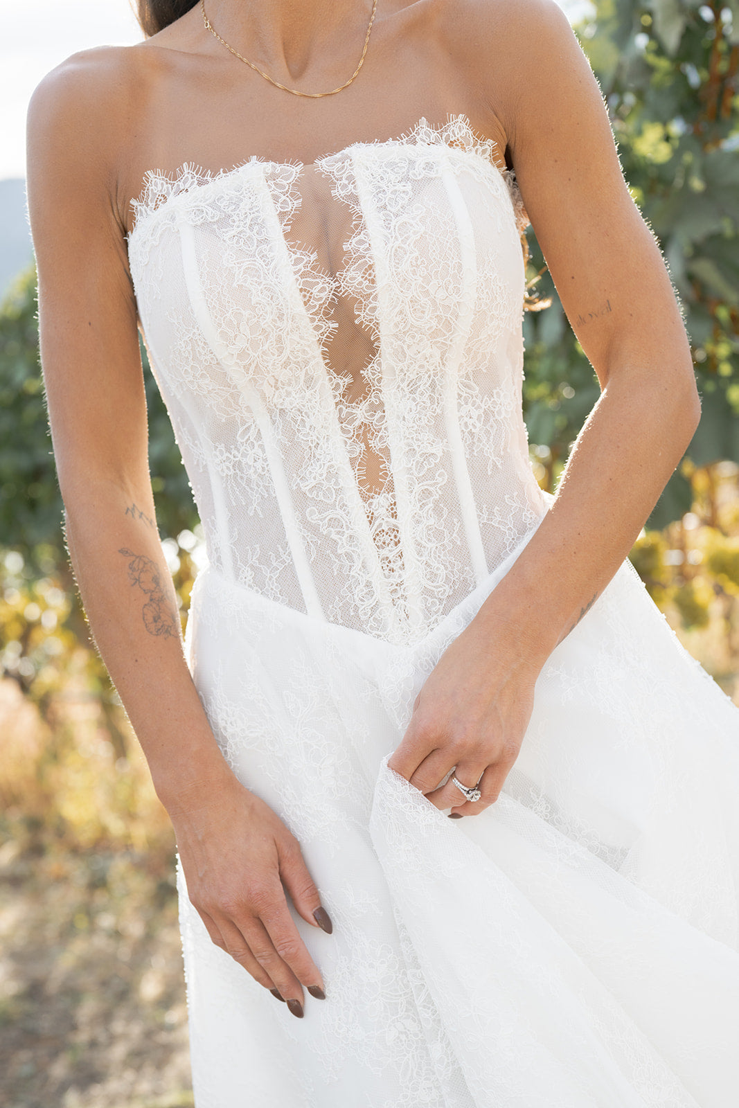 Woman in Amanti Fortuna white wedding dress with Straight across neckline with keyhole detail, Basque waistline for a flattering, elongated shape, A-line silhouette in Chantilly French lace, Zipper back closure for clean lines and comfort dress standing in a vineyard. Le Reve Boutique St. Albert, Alberta
