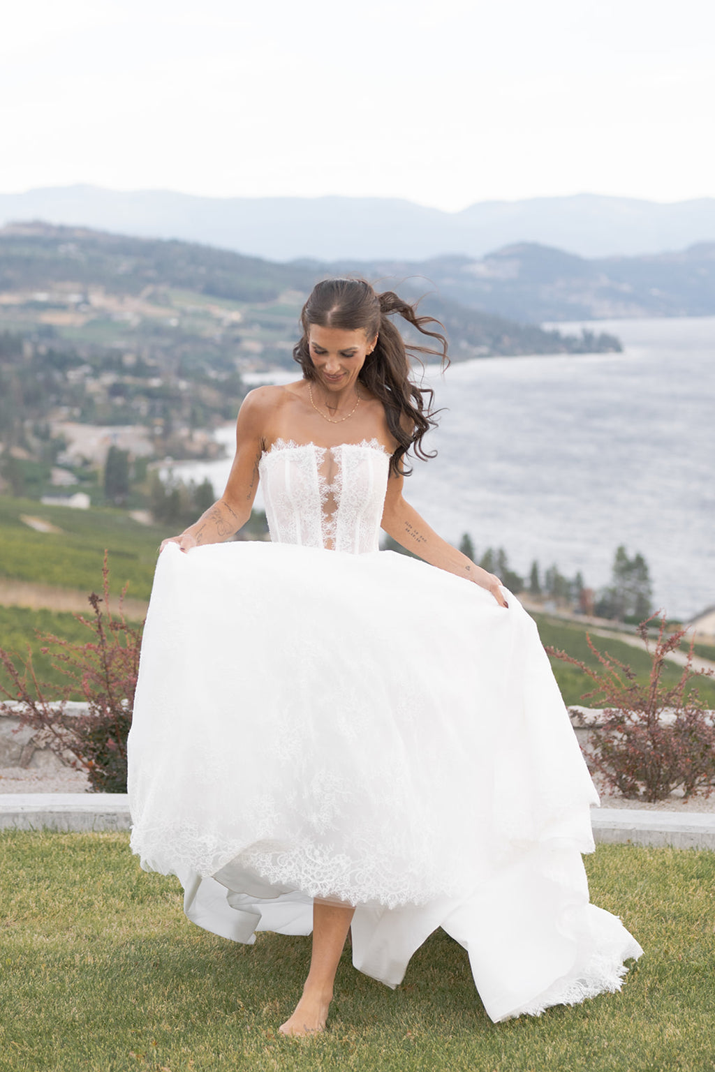 Woman in a Amanti Fortuna A Line white wedding dress standing outdoors with a scenic background.  The modern romantic bride who wants a gown that feels timeless but still fresh, perfect for vineyard weddings, outdoor. ceremonies, and chic celebrations.  Le Reve Boutique Edmonton, Alberta 